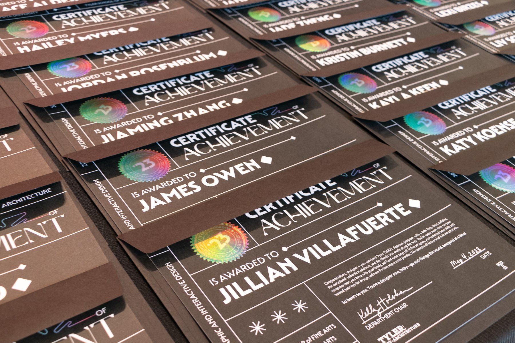 Printed certificates of achievement laid out in rows, each with a holographic class seal