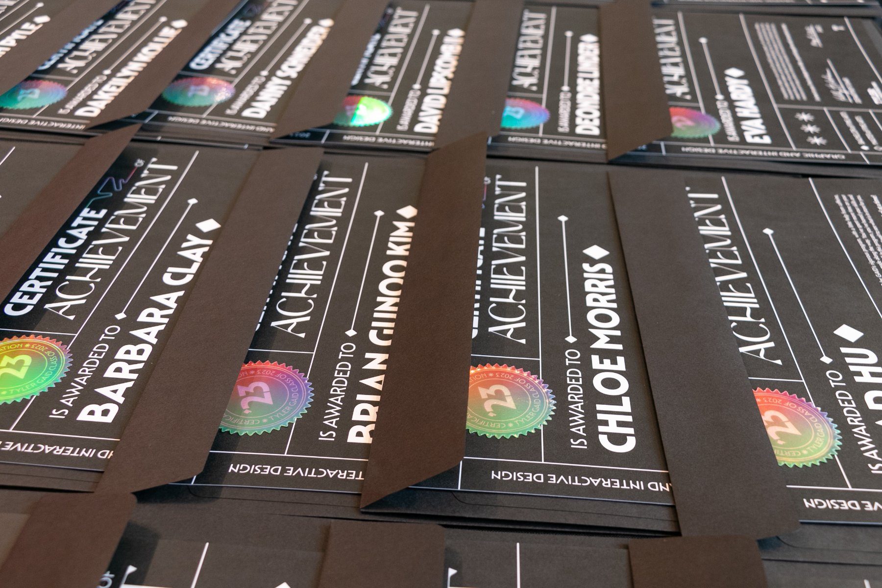 Certificates on dark stock with holographic seals, stacked before sorting